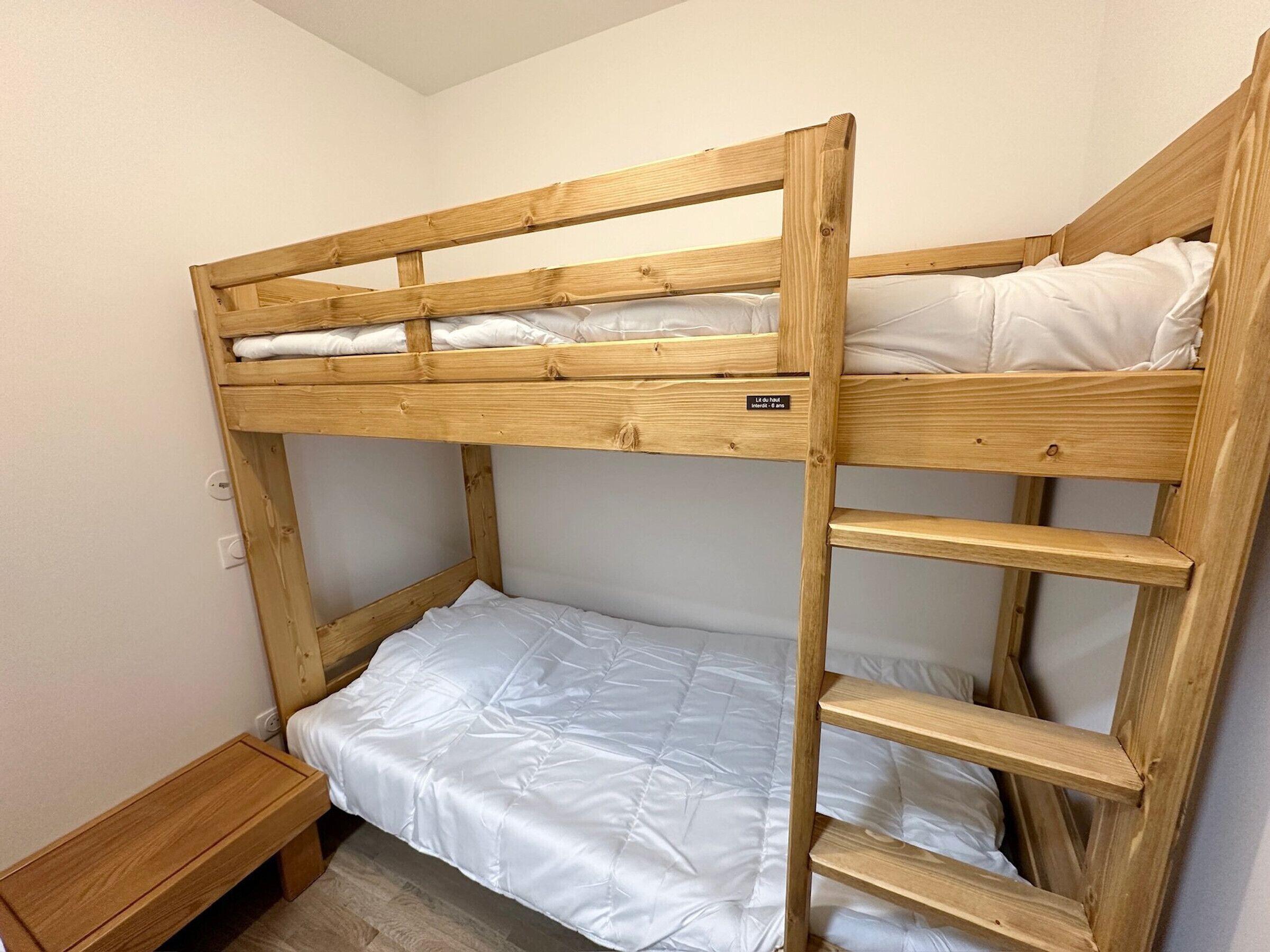Ein Stockbett mit Holzrahmen und weißer Bettwäsche.