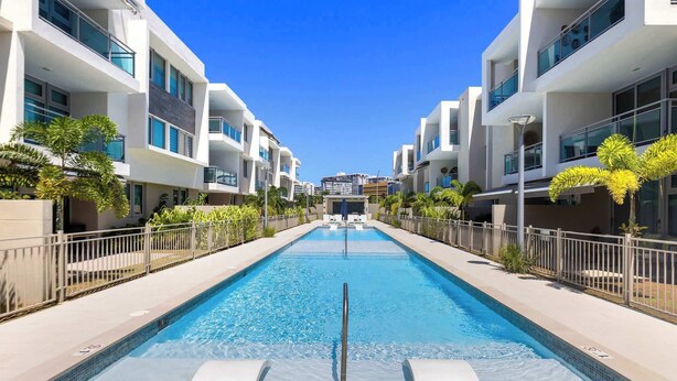 A modern hotel with a central swimming pool, surrounded by balconies and a clear blue sky.