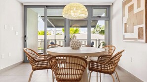 A round dining table with wicker chairs, a woven pendant light, and a decorative vase.