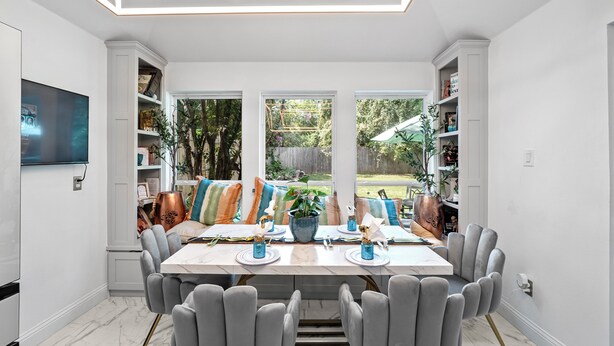 A dining area with a marble table, grey upholstered chairs, and a view of the backyard through large windows. - Cozy 3-bedroom house in welcoming Arlington with WiFi, AC (Arlington)