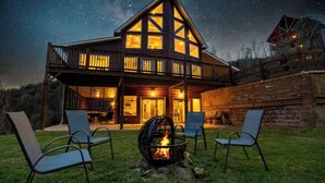 A log cabin with a balcony, a fire pit, and outdoor seating.