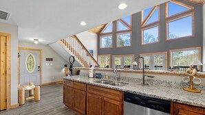 A kitchen with granite countertops, wooden cabinets, a stainless steel dishwasher, and large windows.