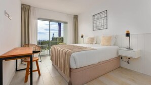 A modern hotel room with a large bed, a desk, and a chair. There is a view of the outdoors through a large window. - Luxury 2-bedroom sea View Apartment in Casares (Casares)