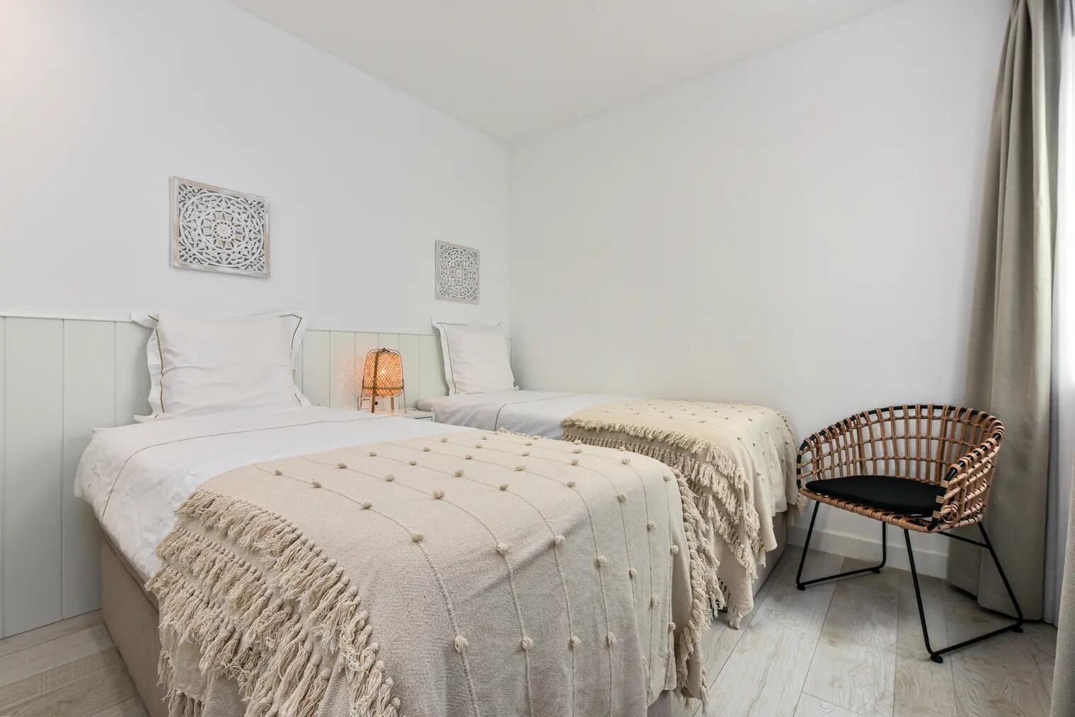 Ein schlicht eingerichtetes Schlafzimmer mit zwei Betten, einem Korbstuhl und Wanddekoration.