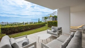 A modern outdoor living area with a sofa set, a small table, and a hammock. - Luxury 2-bedroom sea View Apartment in Casares (Casares)