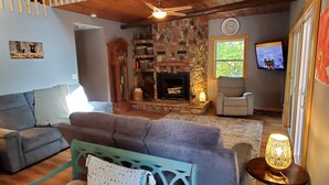 Una sala de estar acogedora con chimenea de piedra, un sofá cómodo, un sillón azul aguamarina y un televisor en la pared.
