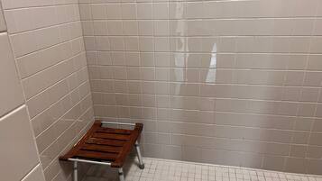 Une salle de bain avec des murs et un sol carrelés de carreaux blancs, un banc en bois et un porte-serviettes en métal.