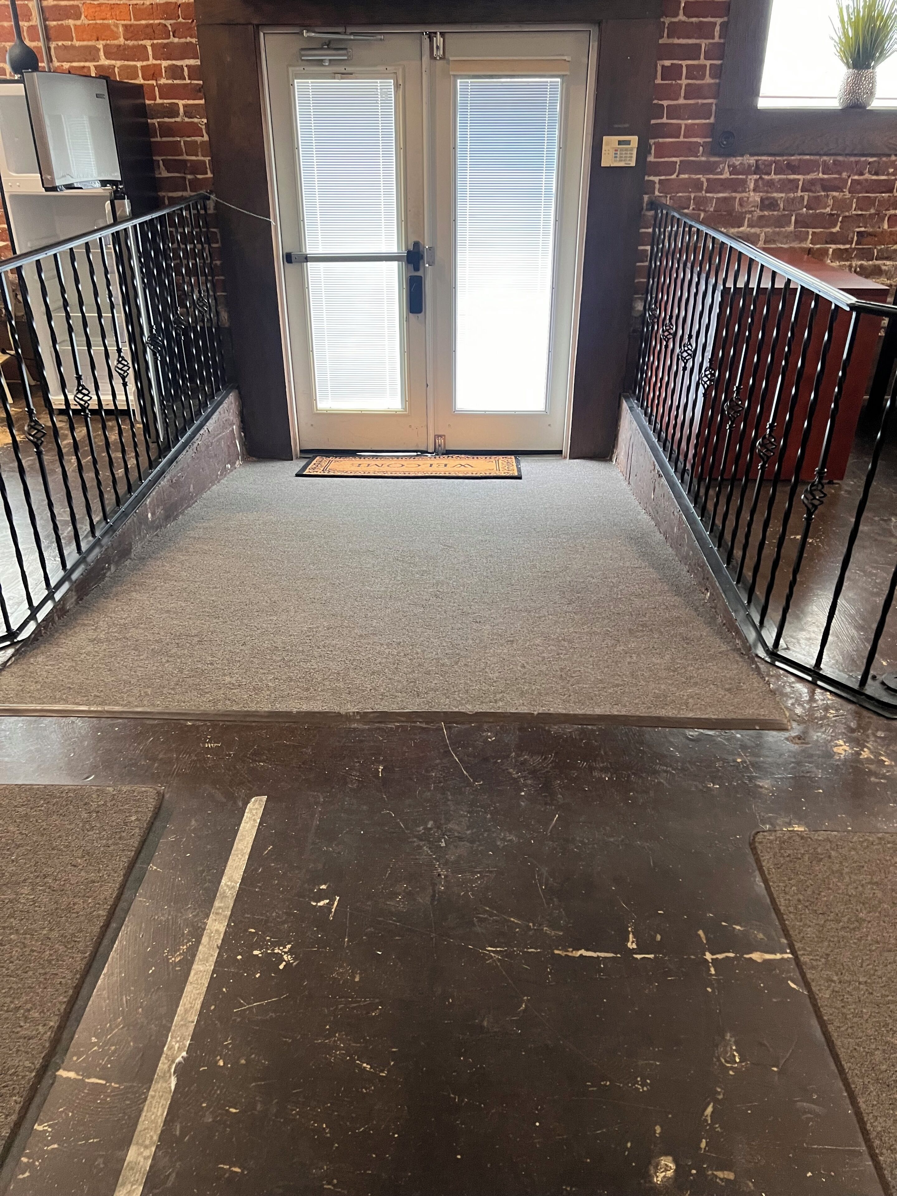 A hotel entrance with a double door, a doormat, and a metal railing.