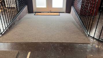 A hotel entrance with a double door, a doormat, and a metal railing.