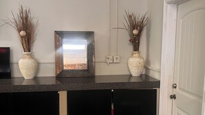 Una cucina con un piano di lavoro in granito, due vasi bianchi con piante essiccate, un quadro incorniciato e una porta bianca.