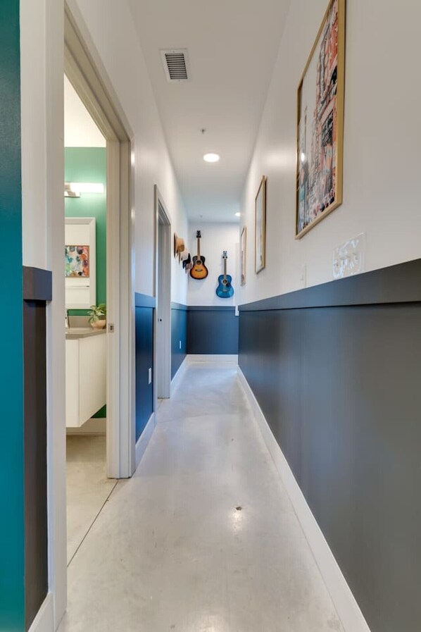 A hallway with a long, narrow corridor, a ceiling vent, and framed artwork on the walls.