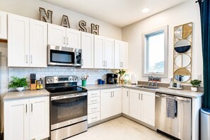 A modern kitchen with white cabinets, stainless steel appliances, and decorative letters spelling 'NASH' on the wall. - King Suite and Spacious Balcony Near Broadway (Nashville)