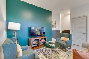 Una sala de estar con paredes color turquesa, un televisor de pantalla plana, un mueble de madera para entretenimiento y dos sillones.