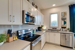 A modern kitchen with stainless steel appliances, white cabinetry, and a window with curtains.