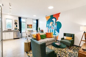 A modern living room with a sofa, armchairs, a coffee table, and a large wall mural.