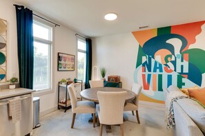 A modern kitchen with a round dining table, chairs, a built-in oven, and a window with curtains.