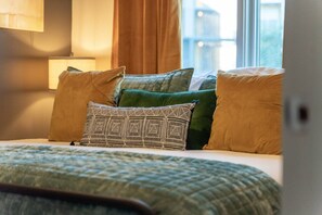 A bed with a green quilt, multiple pillows, a patterned pillow, and a window with curtains.