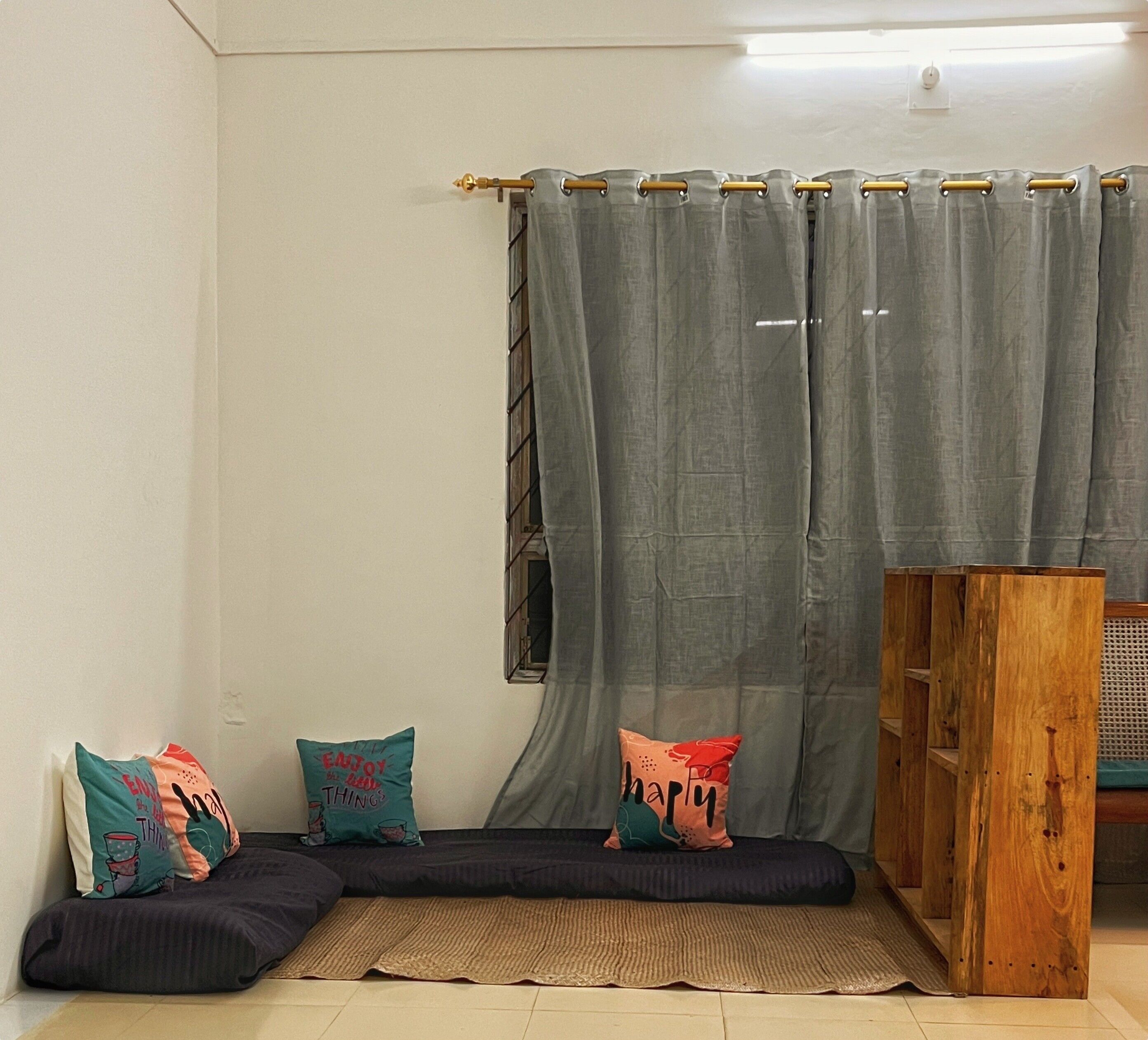 Una habitació acollidora amb un sofà seccional, almofades decoratives, un armari de fusta i una cortina gris.