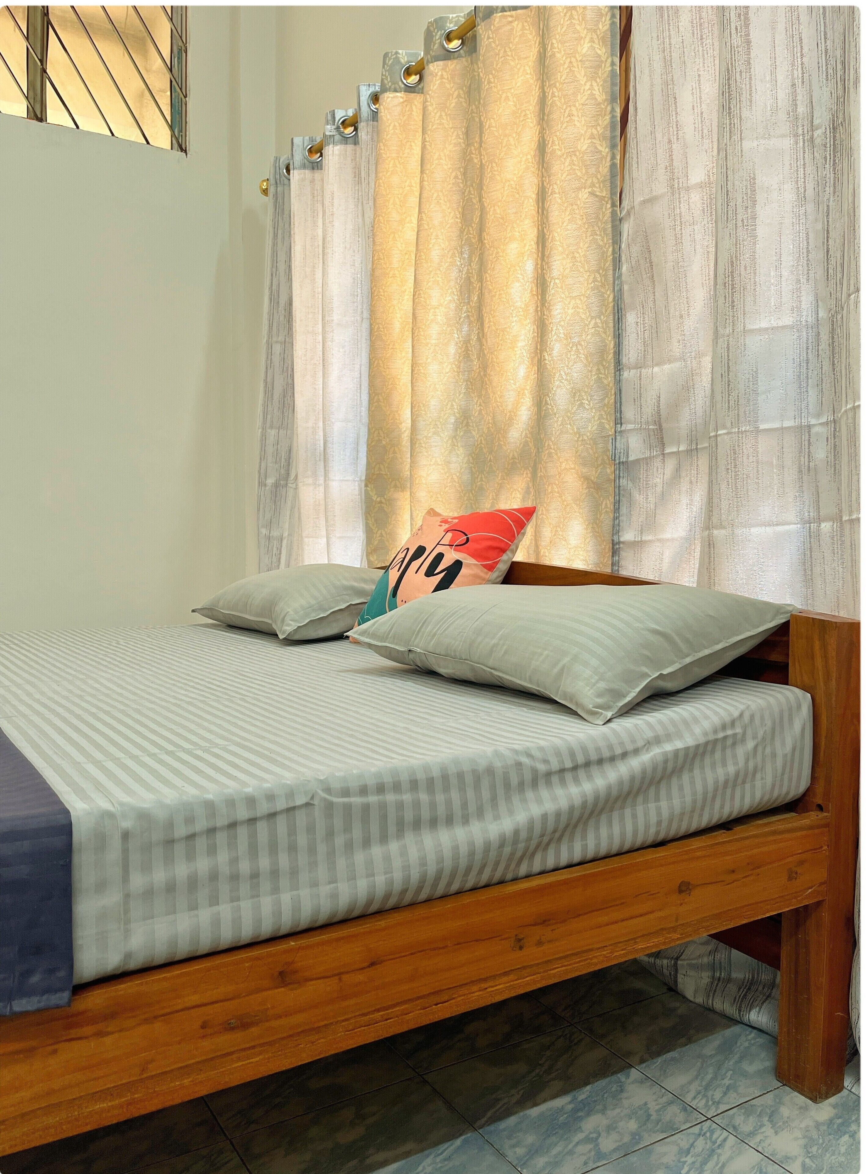 A wooden bed with striped bedding and a pillow with a 'happy' design.