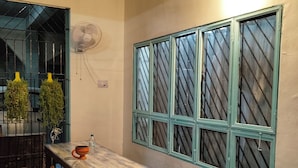 A dining area with a wooden table and benches, a wall-mounted fan, and a window with a grid pattern. - zion backpackers hostel (Guwahati)