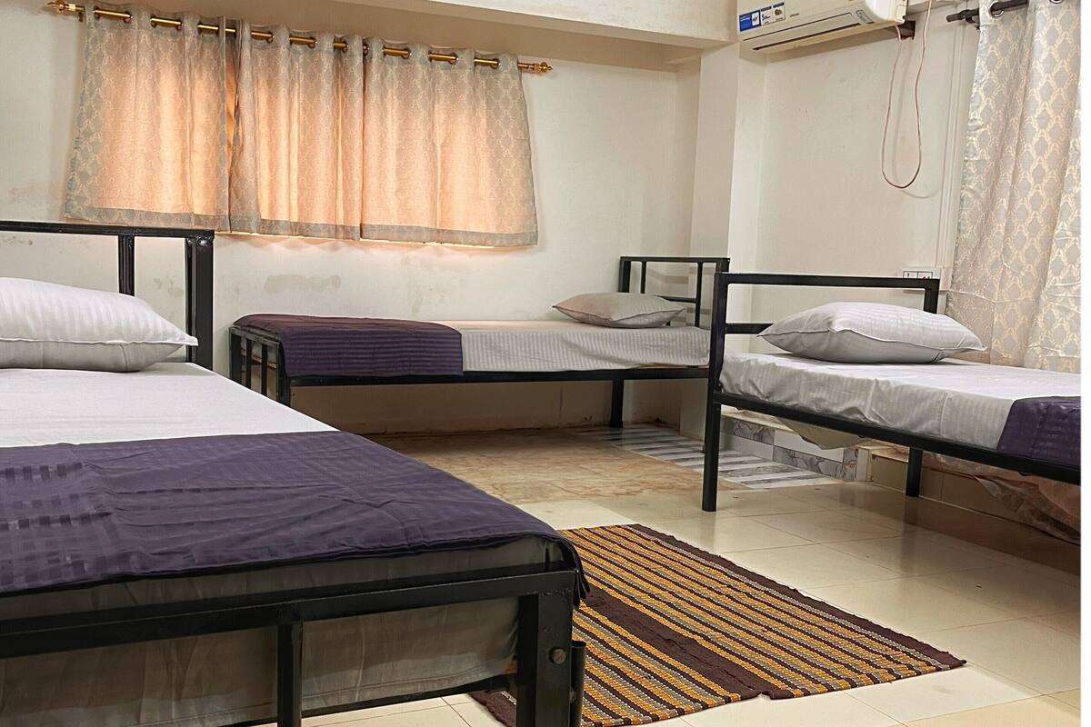 A room with three beds, a window with curtains, an air conditioning unit, and a tiled floor.