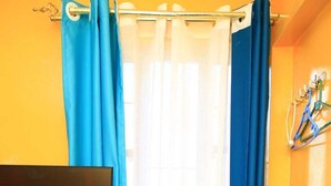 A room with a bed, a television mounted on the wall, and a window with blue curtains. - Superhighway Haven, 2 Mins To SpurMall Kimbo-Ruiru,  EXIT 12&13 Thika Road (Kimbo, Ruiru)