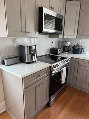 Cozinha moderna com eletrodomésticos de aço inoxidável, micro-ondas, máquina de café, torradeira e forno.