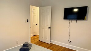 Quarto com uma cama, televisão presa na parede e porta para outro espaço.