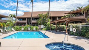 A swimming pool with lounge chairs, a hot tub, and a building with balconies and palm trees.