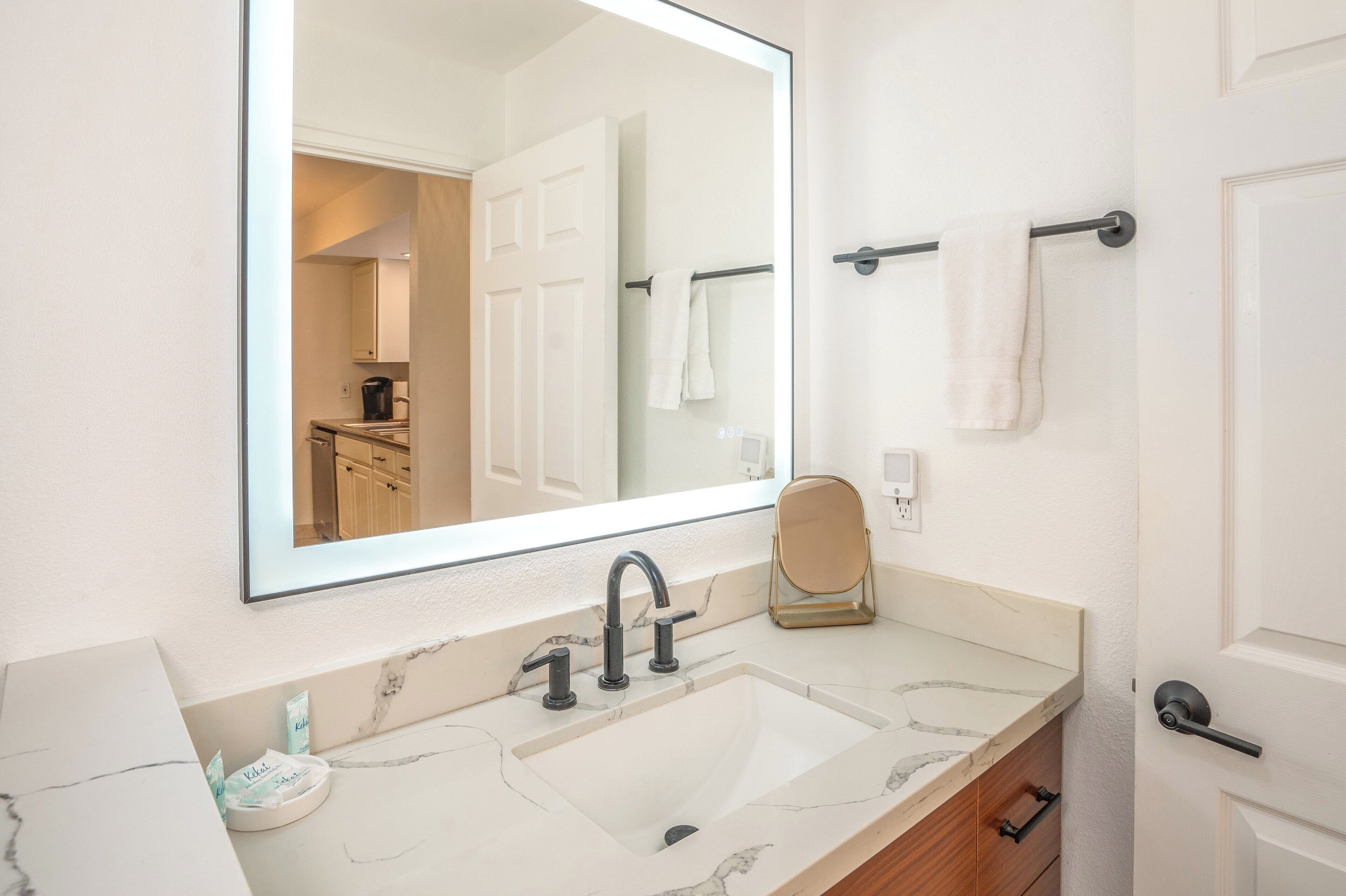 Un baño con un espejo grande, un lavabo con encimera de mármol, un perchero y una puerta.
