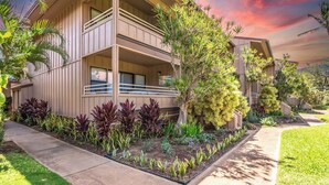 A two-story building with a balcony on the second floor, surrounded by a landscaped garden with various plants and a well-maintained lawn.