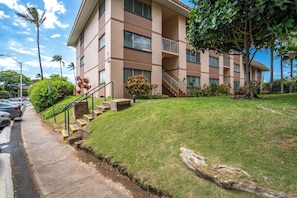 A multi-story building with a flat roof, a staircase leading to the entrance, and a well-maintained lawn. - Kihei Kai Nani #6-349 Remodeled End Unit, Across Kamaole Beach II, Ocean View (Kihei)