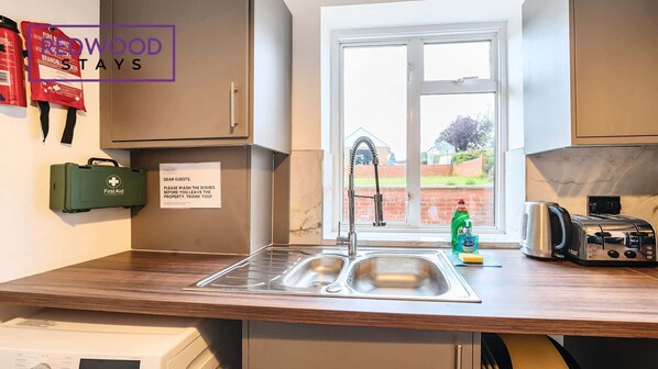 A modern kitchen with a sink, a first aid kit, and a note asking guests to wash dishes.
