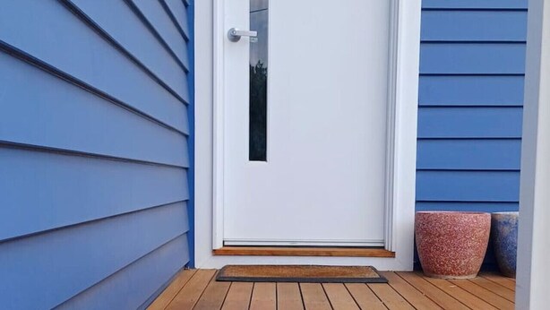 A white door with a small window, a doorknob, and a wooden deck in front. - Ocean Blue - Linen,  WiFi, Kayo and Pet Friendly (Venus Bay)