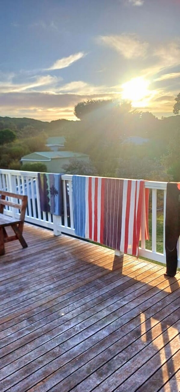 A wooden deck with a railing, a bench, and a view of a sunset over a landscape.