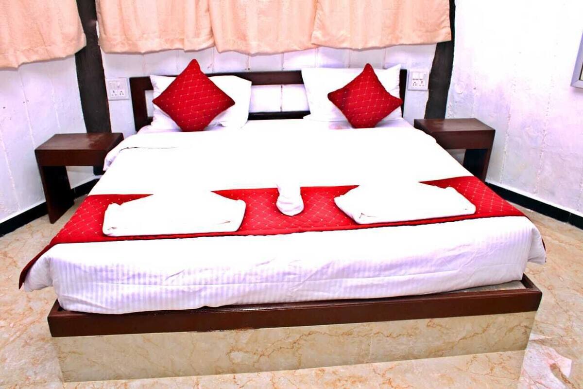 Una cama bien hecha con ropa de cama roja y blanca, dos mesitas de noche y un suelo de mármol.