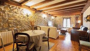 A cozy room with stone walls, wooden beams, a dining table with chairs, and a sofa. - Zelaikoa Goikoa - baskeyrentals (Zestoa)