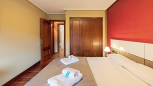 A hotel room with a bed, two towels, a nightstand, a lamp, and wooden doors. - Zelaikoa Goikoa - baskeyrentals (Zestoa)
