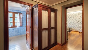 A hallway with wooden doors, a bathroom with a bamboo wallpaper, and a view of a bathroom with a toilet and blue tiles. - Zelaikoa Goikoa - baskeyrentals (Zestoa)