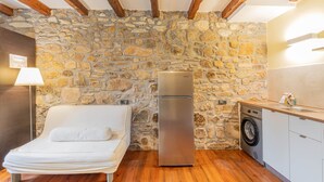 Un dormitorio con pared de piedra, una cama, un refrigerador y una lavadora.