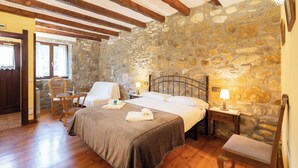 A bedroom with a stone wall, wooden beams, a bed, bedside tables, and a chair.