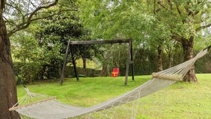 A hammock tied between trees in a grassy area with a wooden swing set in the background.