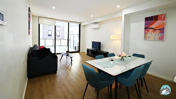 A modern living room with a sofa, a dining table with chairs, a TV, and a large window. - Comfortable 2 Bed Apartment in Canterbury (Canterbury)