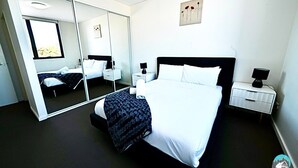 A modern hotel room with a large bed, a bedside table, a nightstand, a mirror, and a window. - Comfortable 2 Bed Apartment in Canterbury (Canterbury)