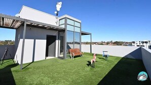 A modern building with a glass facade, a covered patio area with artificial grass, and a clear blue sky. - Comfortable 2 Bed Apartment in Canterbury (Canterbury)