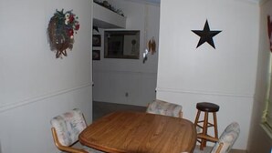 A dining area with a wooden table and four chairs, a black star decoration on the wall, and a small stool.