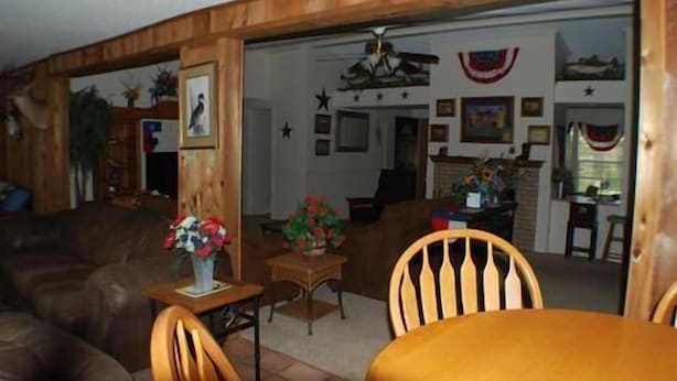 A cozy living room with a wooden ceiling, a dining area with a table and chairs, and a kitchen visible through an open doorway.