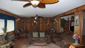 A rustic living room with a large leather sofa, wooden walls, and a ceiling fan.