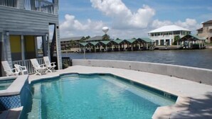 A swimming pool with lounge chairs, a water view, and a building with a white exterior and a green roof. - Pelican Point #4 - Great Complex! Great Views! Cool off in the swimming pool! (Port Mansfield)