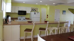 A kitchen with white cabinets, a microwave, a stove, and a refrigerator. There are two white chairs and a wooden table. - Pelican Point #4 - Great Complex! Great Views! Cool off in the swimming pool! (Port Mansfield)